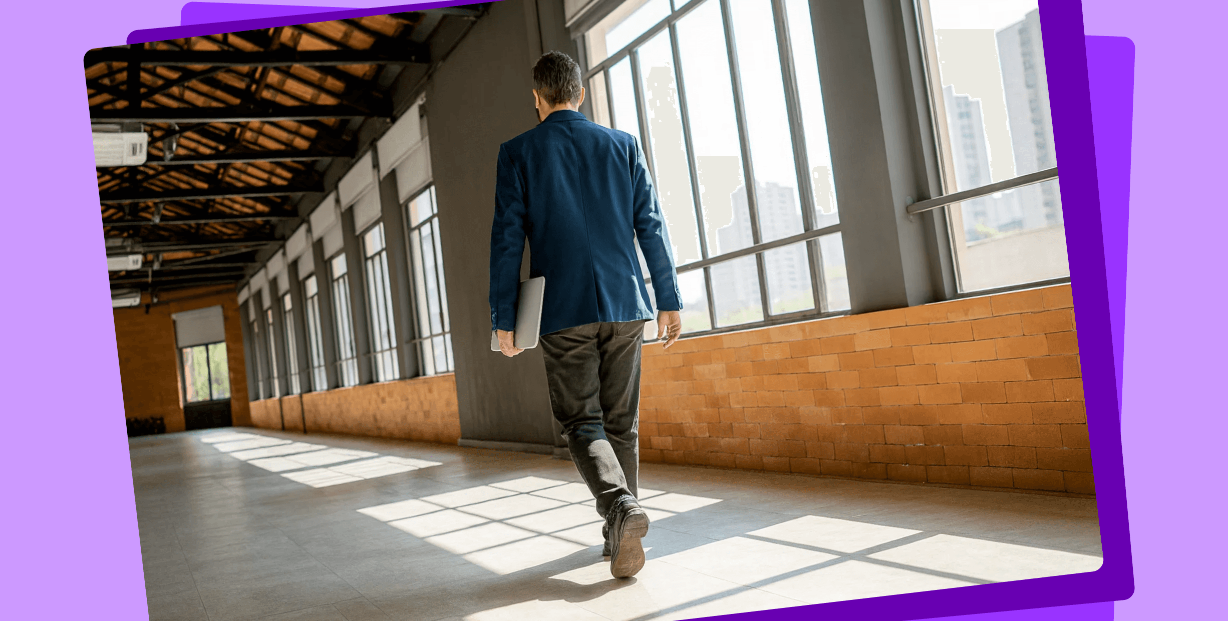 A man carrying a laptop and walking through a hallway in an office building